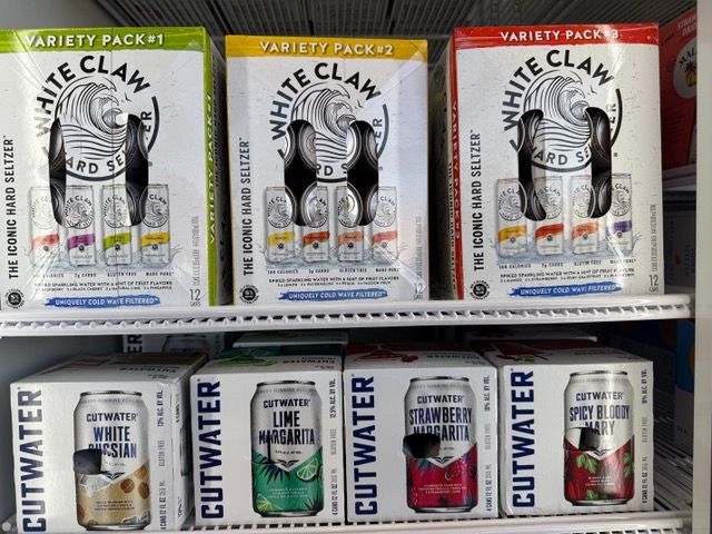 White Claw and Cutwater hard seltzer variety packs in a refrigerator.
