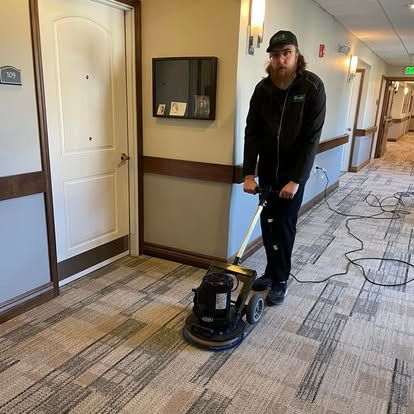 A person using a floor buffer to clean a carpeted hallway.