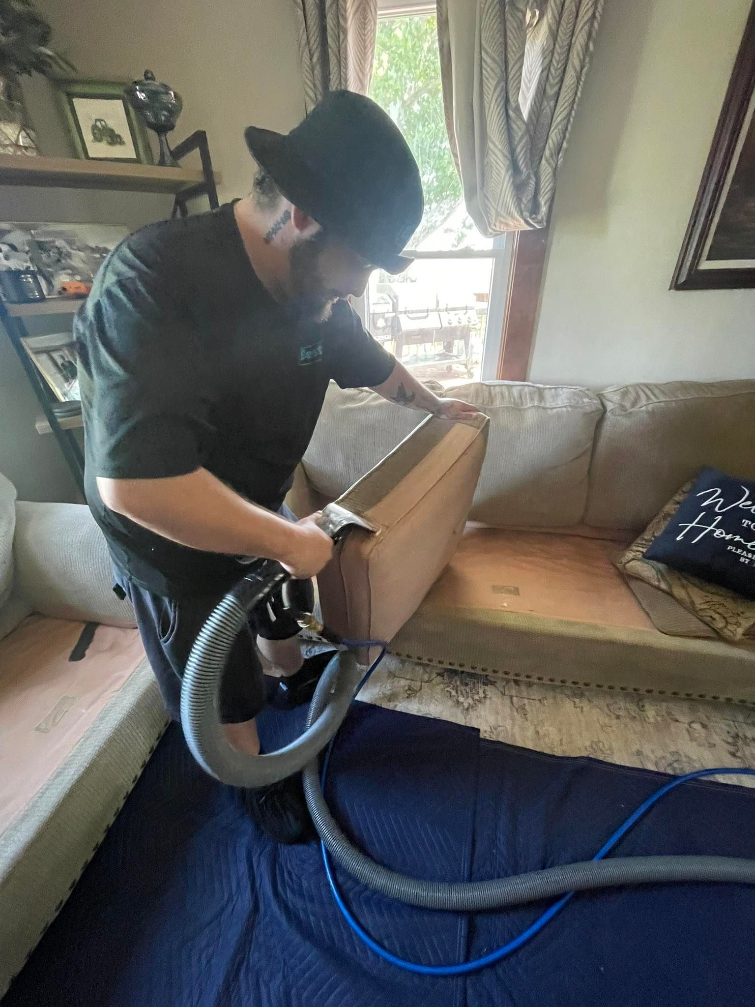 Person vacuuming a sofa with an upholstery cleaner in a living room.