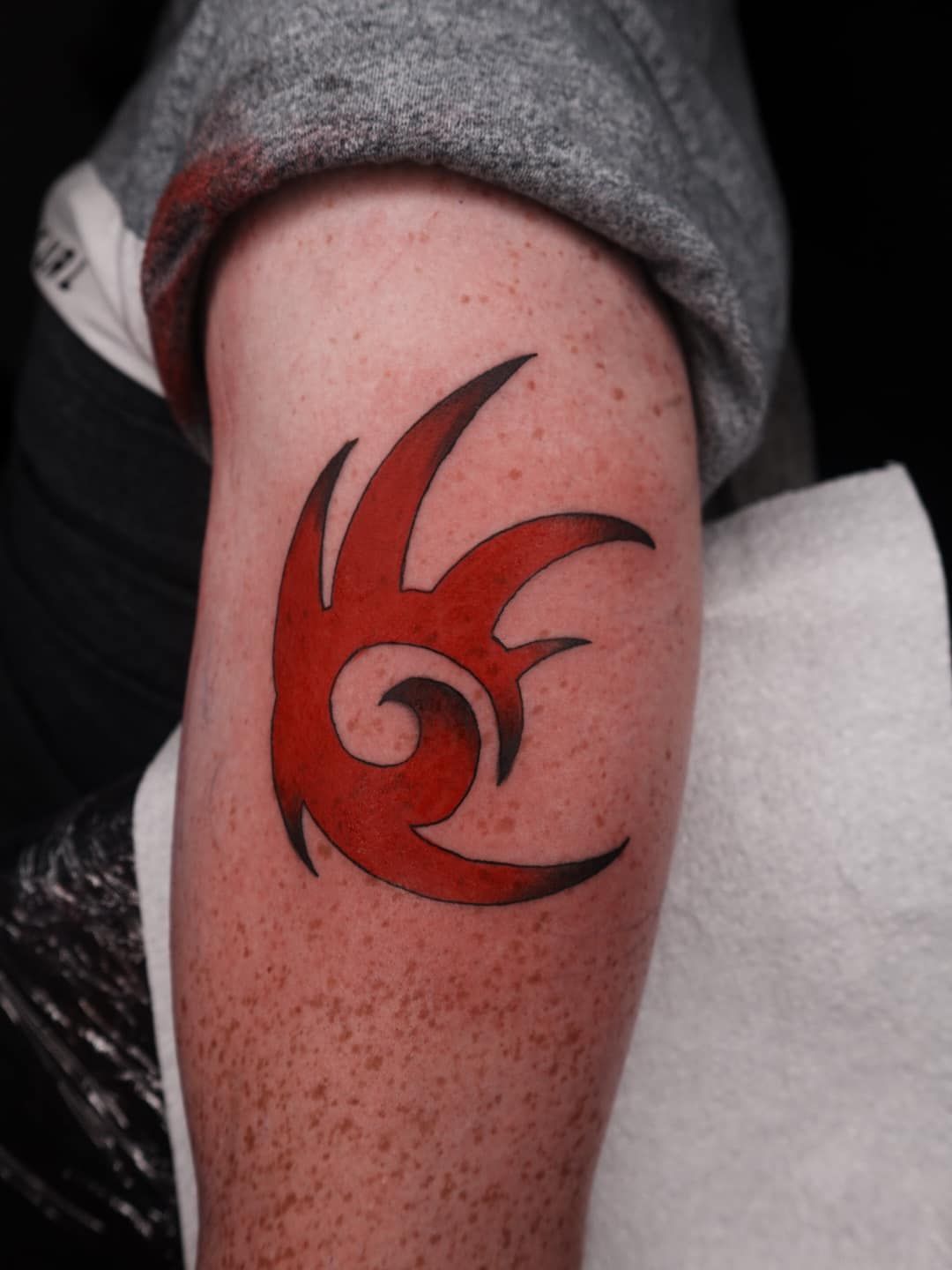 Red Tattoo of A Stylized Flame Design on A Freckled Arm, with A Gray Sleeve Visible — Thaiger Ink In Holloways Beach, QLD