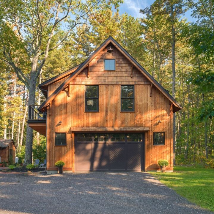 Two-story wooden garage with dark gray door, set among trees.