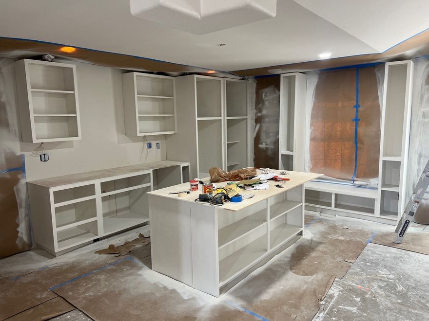 Kitchen under renovation with white cabinets, central island, and construction materials on the floor