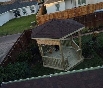 Wooden gazebo with brown roof in a backyard.