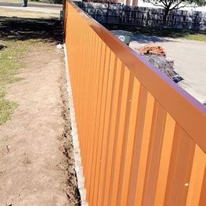 Orange metal fence next to a dirt path and a road.