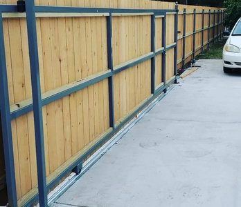 Wooden fence with dark metal frame and sliding gate, next to a concrete driveway.