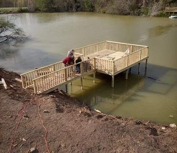Wooden pier extending into a murky lake, with two people on the ramp and deck.
