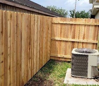 Wooden fence surrounds a yard with an air conditioning unit.