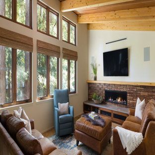 Living room with leather sofas, stone fireplace, and tall windows overlooking trees.