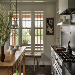 Kitchen with a wooden table, stove, and two windows with a bench, sunlight, and a vase of plants.