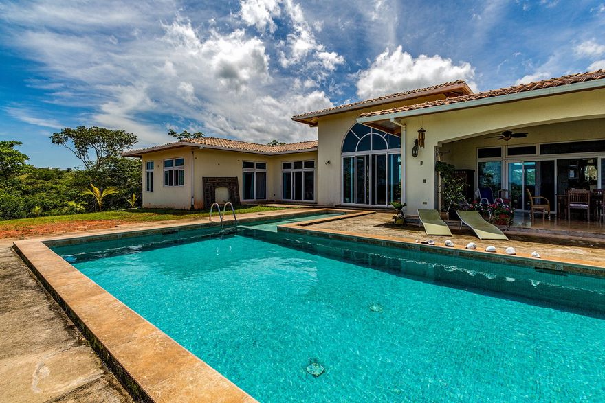 Backyard swimming pool beside a villa under a blue, cloudy sky