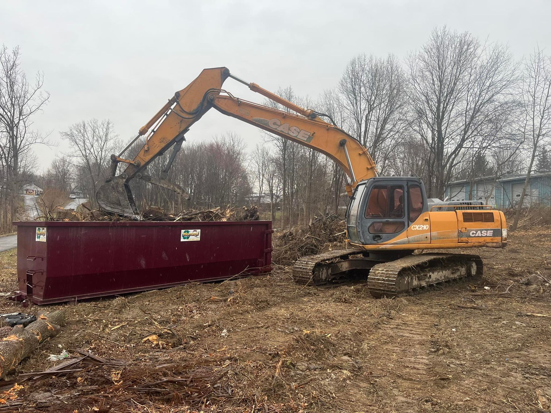An excavator is loading a dumpster with dirt in a field.