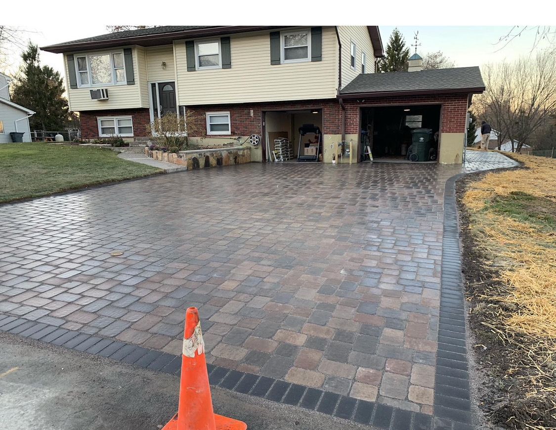 A brick driveway with a traffic cone in front of a house.
