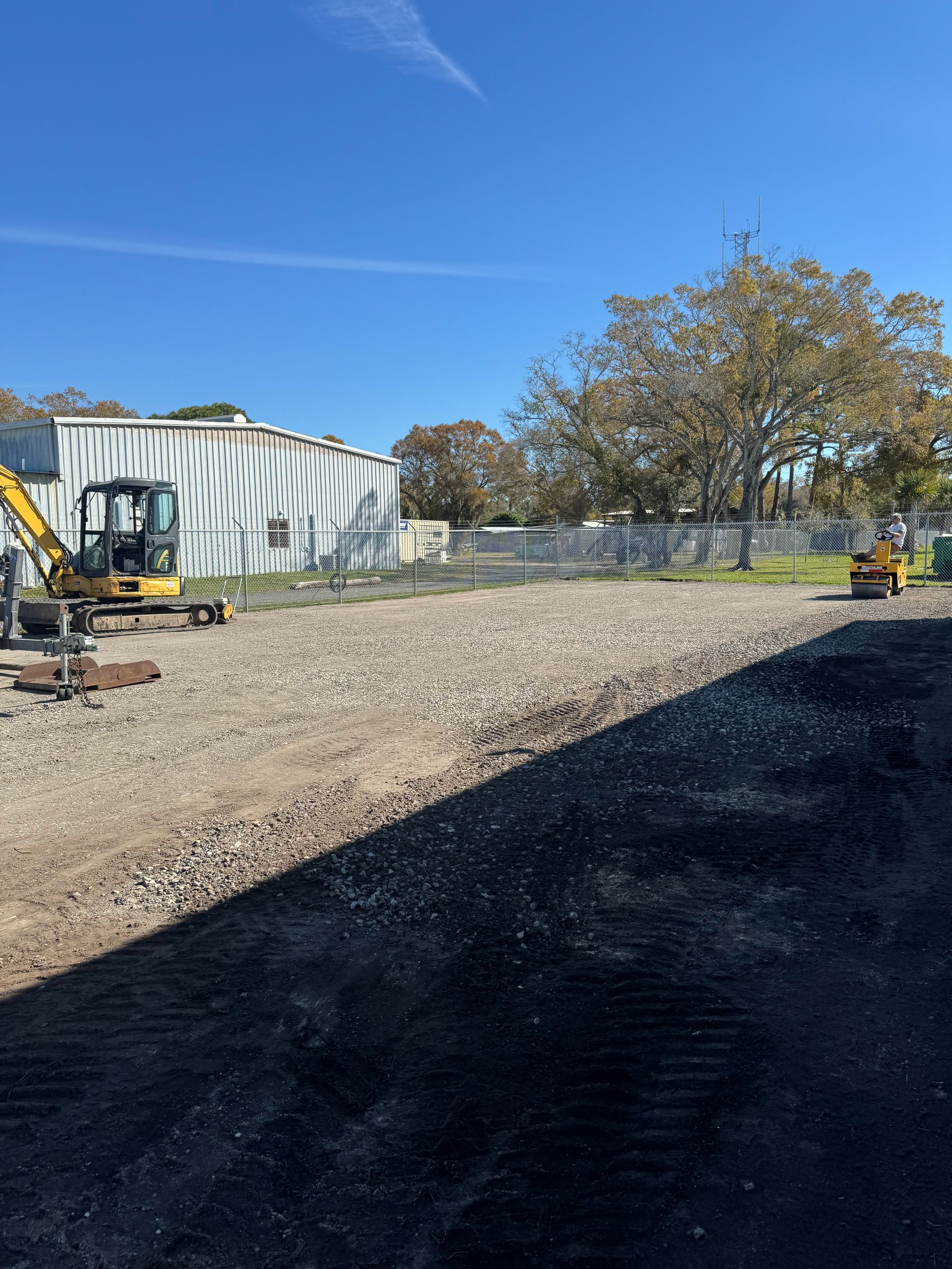 A yellow excavator is parked in a gravel lot in front of a building.