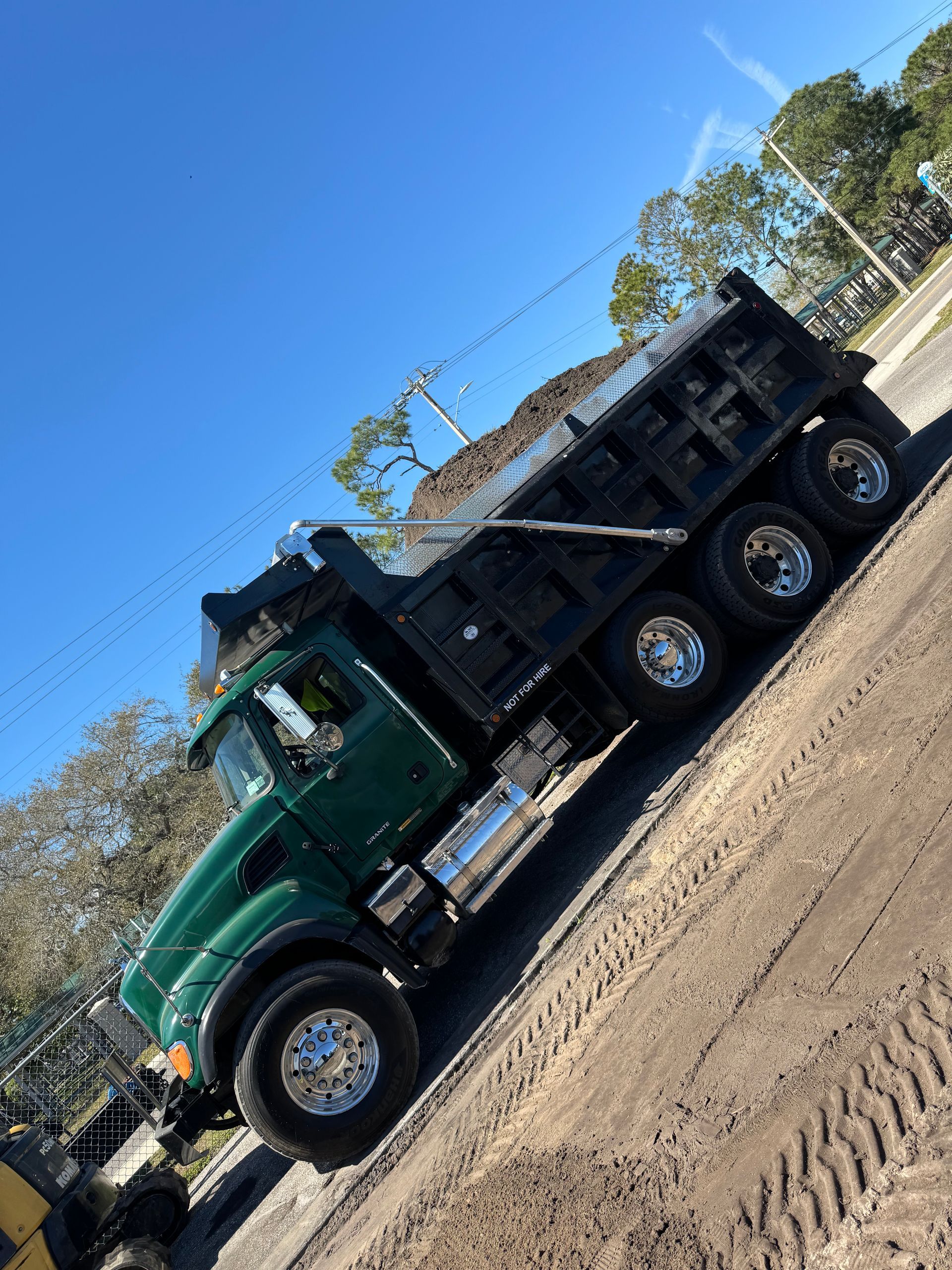 A green dump truck is parked on a dirt road.