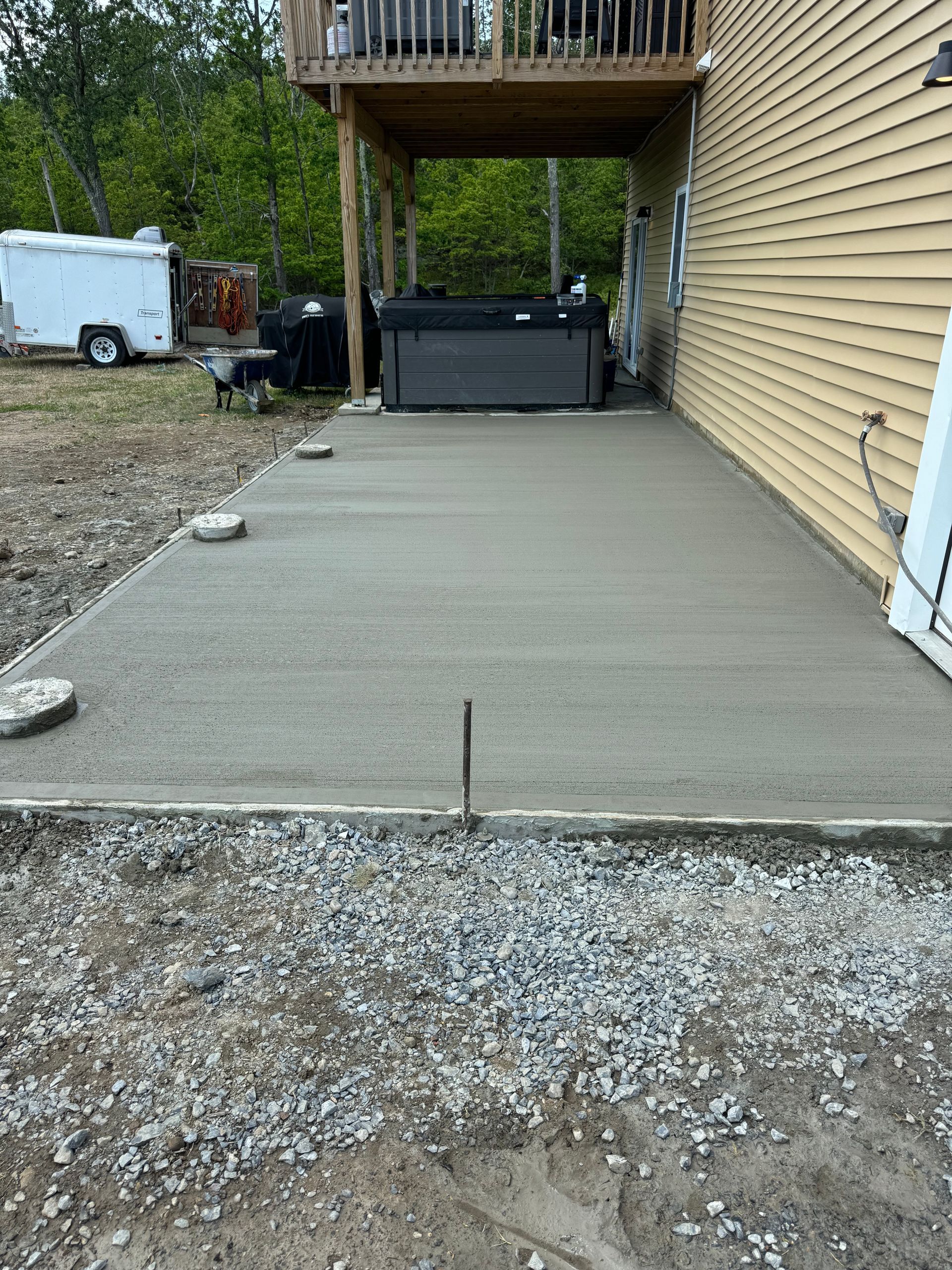 A concrete patio is being built in front of a house with a hot tub underneath it.