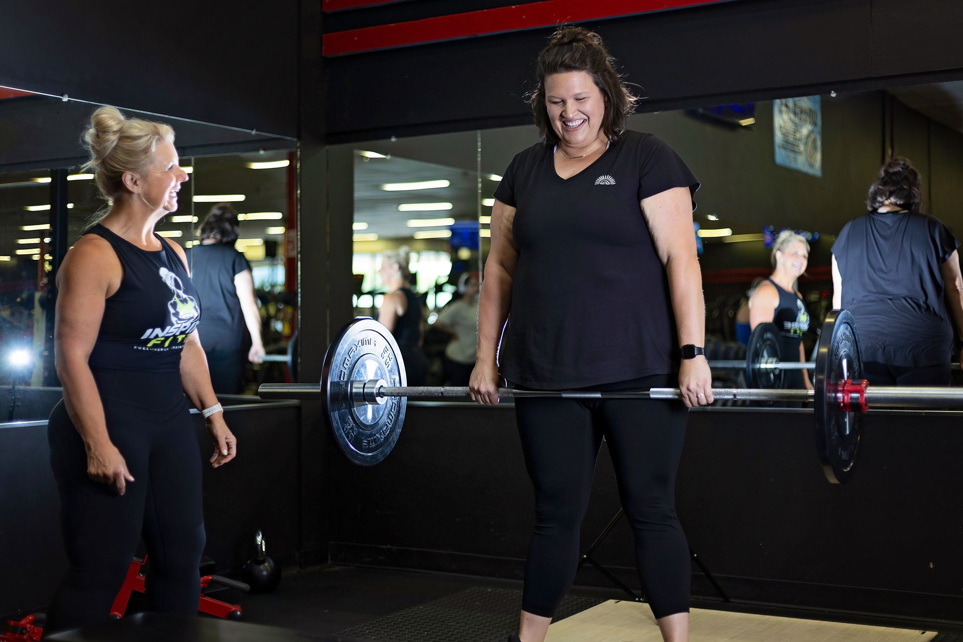 Two women are standing next to each other in a gym holding a barbell.