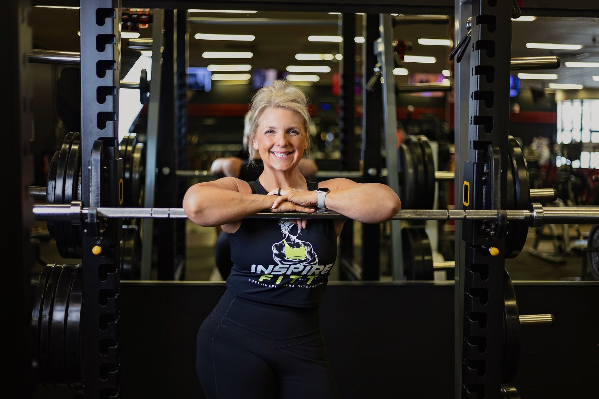 A woman is standing in front of a barbell in a gym.