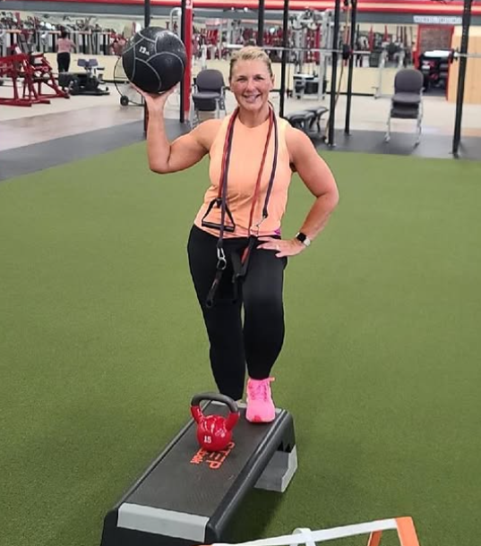 A woman is standing on a bench in a gym holding a ball