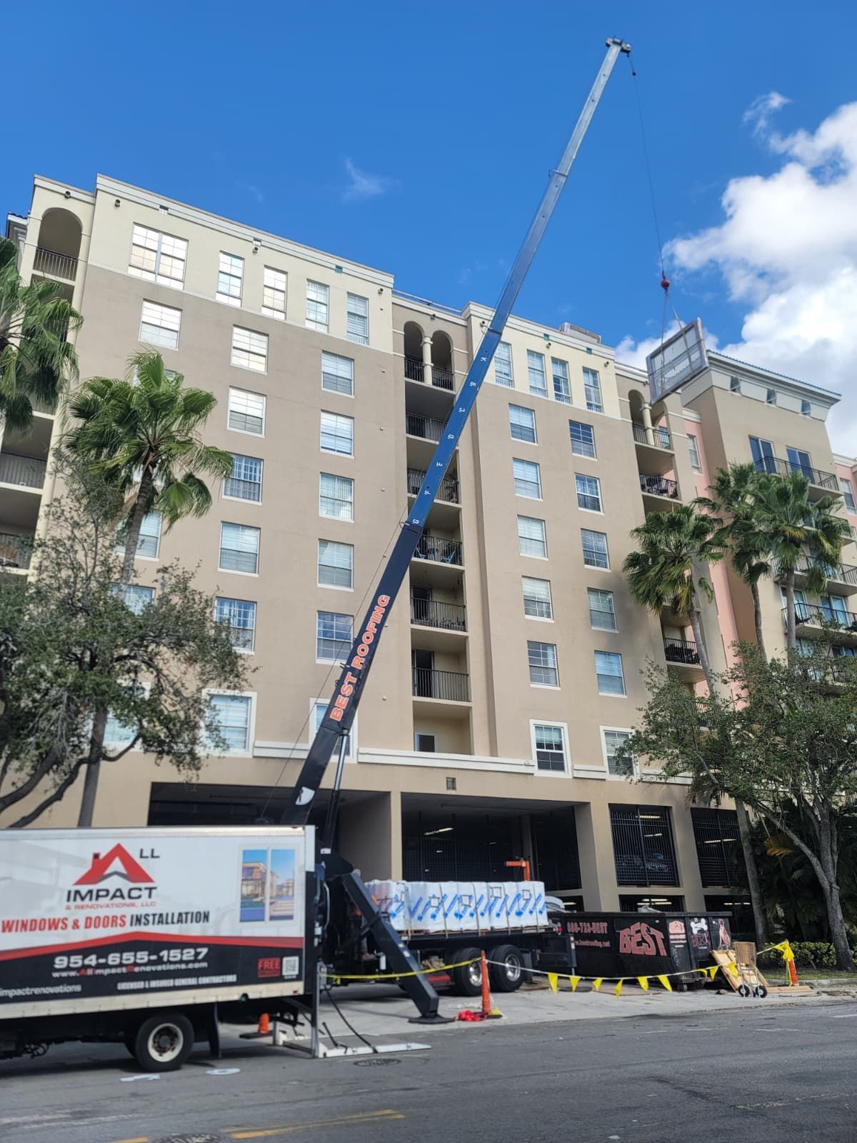 A crane lifts impact window materials onto the rooftop of a commercial building in Broward County.