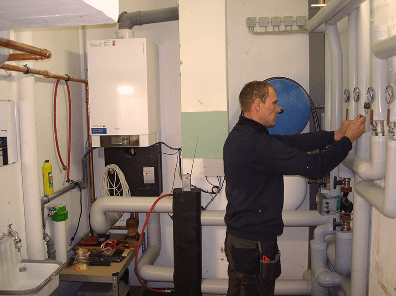 Ein Mann arbeitet an einem Heizkessel in einem Raum mit Rohren