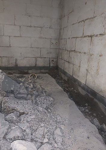 Concrete block walls and floor with debris, a dark band along the wall, and construction materials.
