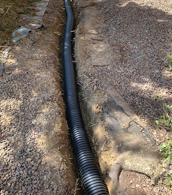 Black corrugated pipe installed in a trench surrounded by gravel and soil.