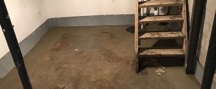 A concrete basement with wooden stairs, showing dirt and stains on the floor and stairs.