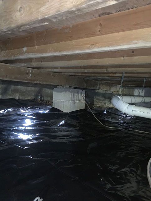 View of a crawl space with black plastic covering the ground. Wood beams above.