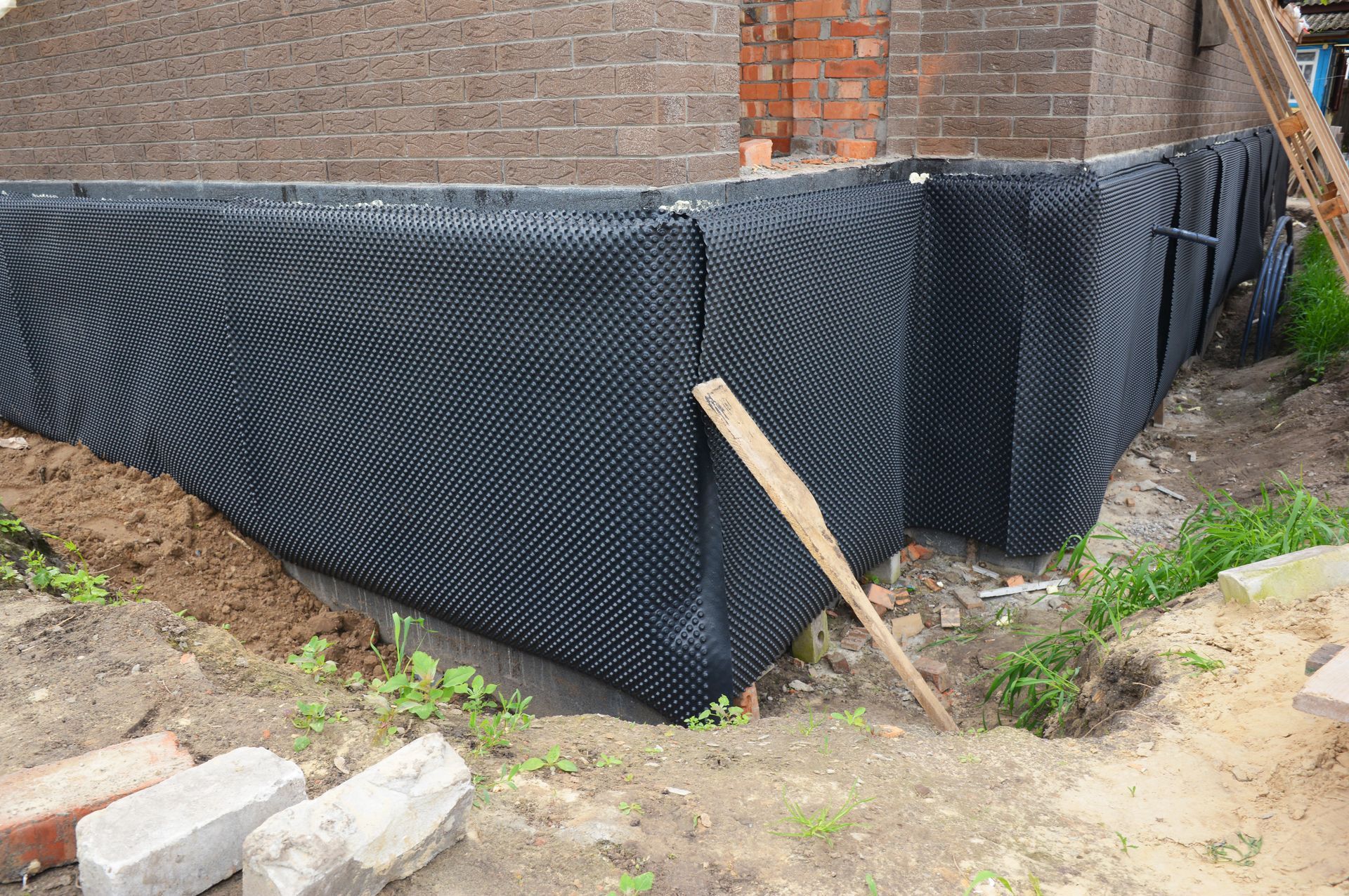 Black drainage membrane installed on the foundation of a brick building.