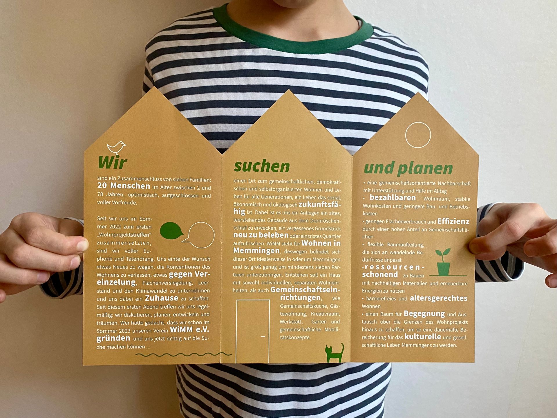 Eine Person in einem gestreiften Hemd hält ein Stück Papier in der Form eines Hauses.