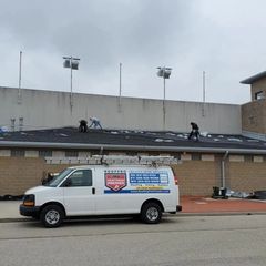 Three workers repair a dark shingled roof while a white 