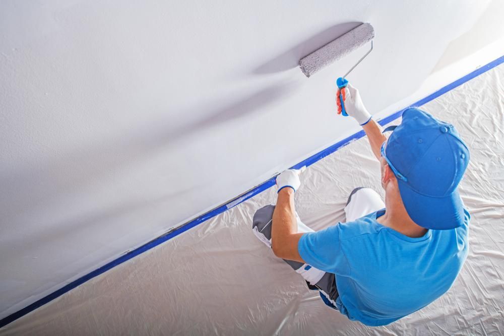 A Man is Sitting on the Floor Painting a Wall With a Paint Roller — Cutting Edge Painting Contractors QLD in Goomboorian, QLD