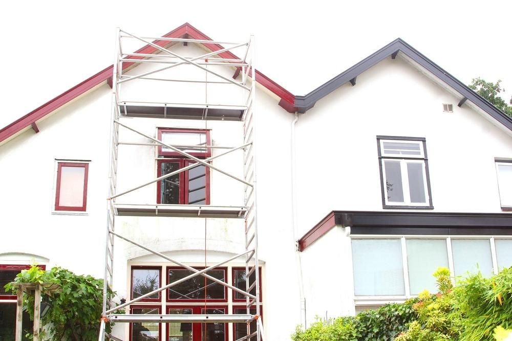 A White House With a Red Roof and a Scaffolding in Front of It — Cutting Edge Painting Contractors QLD in The Dawn, QLD