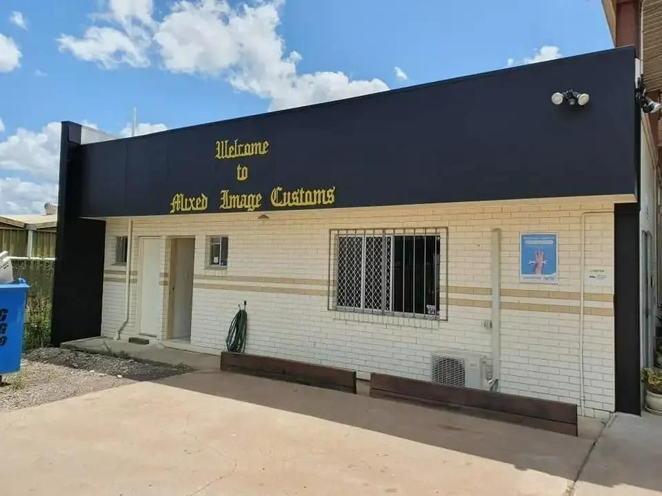 A White Brick Building With a Black Sign That Says Welcome to Mad Image Customs — Cutting Edge Painting Contractors QLD in Veteran, QLD