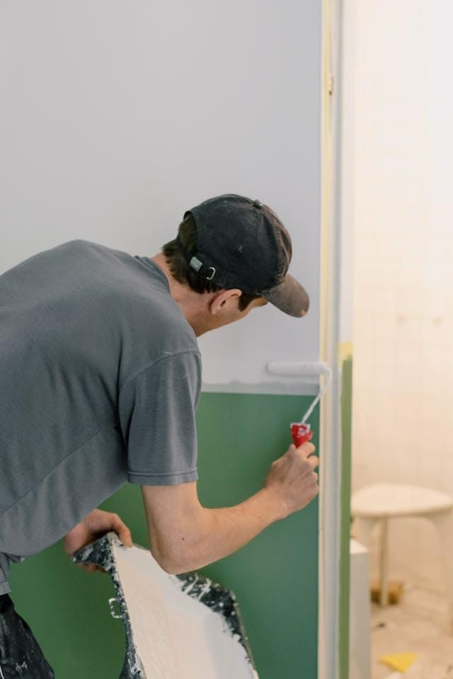 A Man is Painting a Wall in a Bathroom With a Screwdriver — Cutting Edge Painting Contractors QLD in Chatsworth, QLD