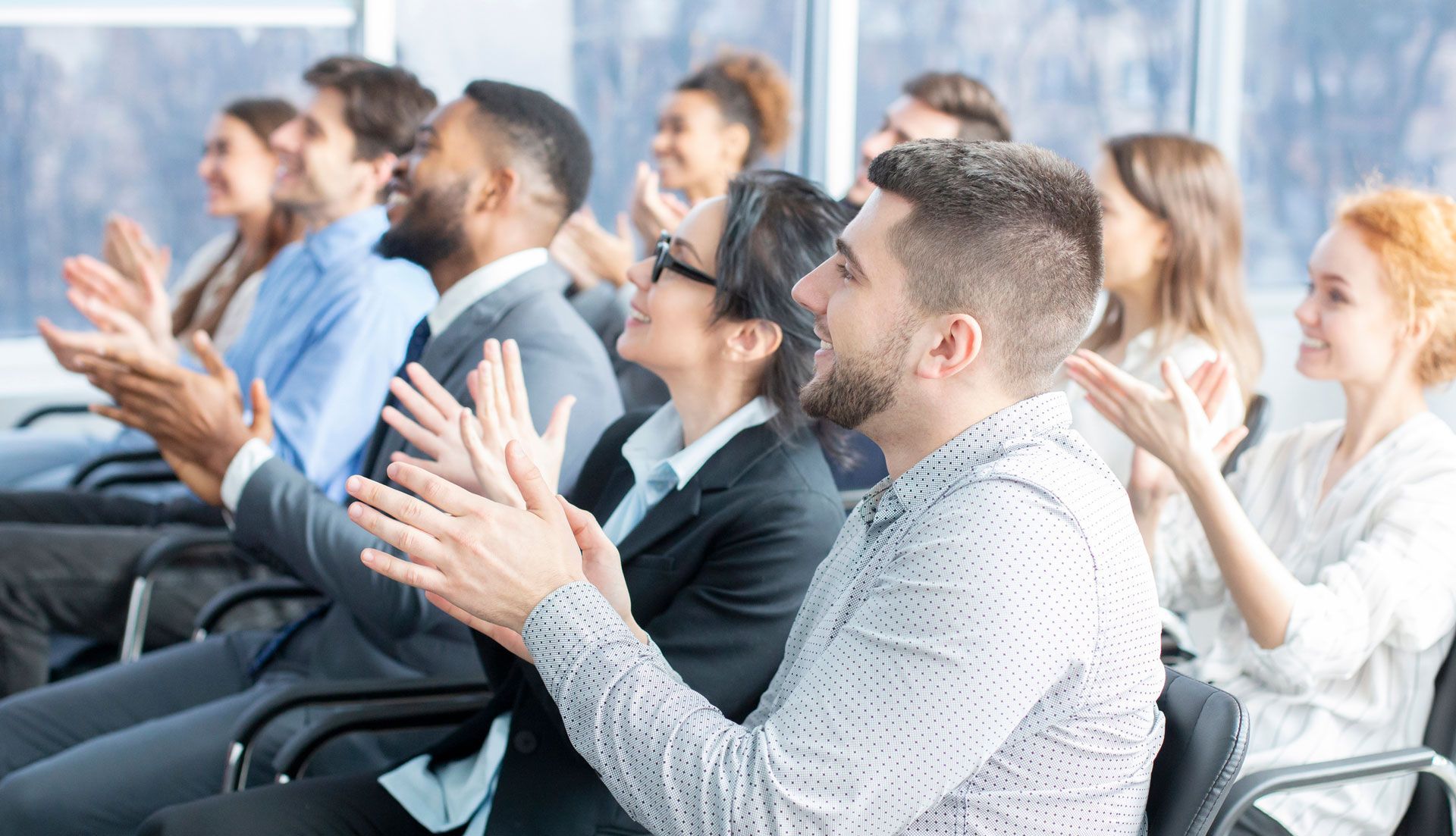 People clapping in a well-lit conference room, likely after a presentation.