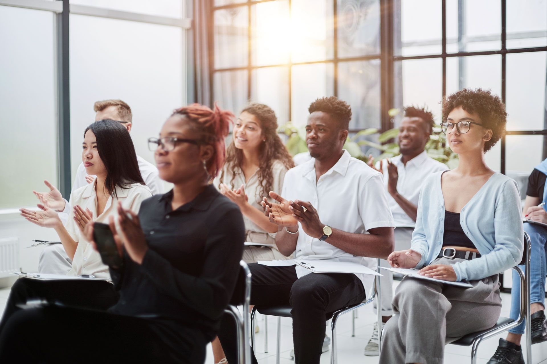 People applauding in a bright room with large windows, some holding notebooks.