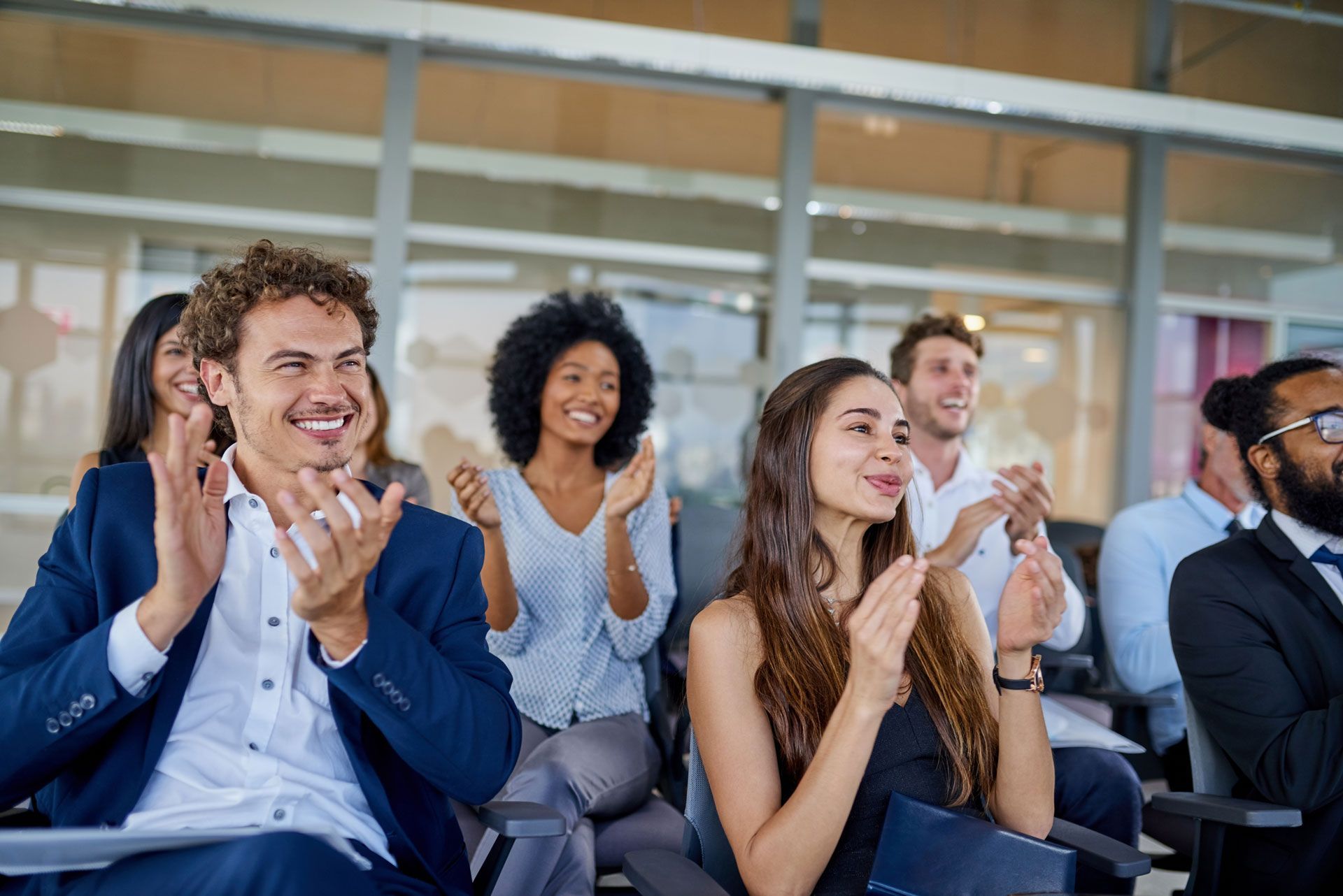 People in business attire applaud in a modern conference room.
