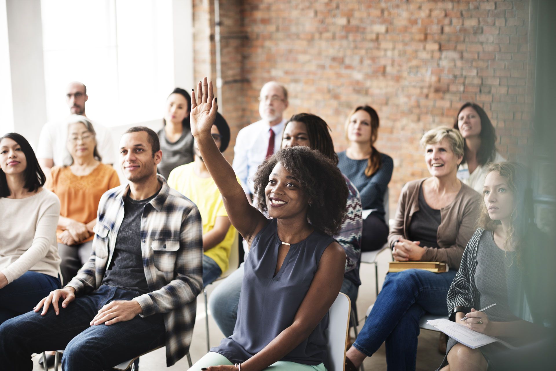 Audience in a meeting with a woman raising her hand to ask a question.