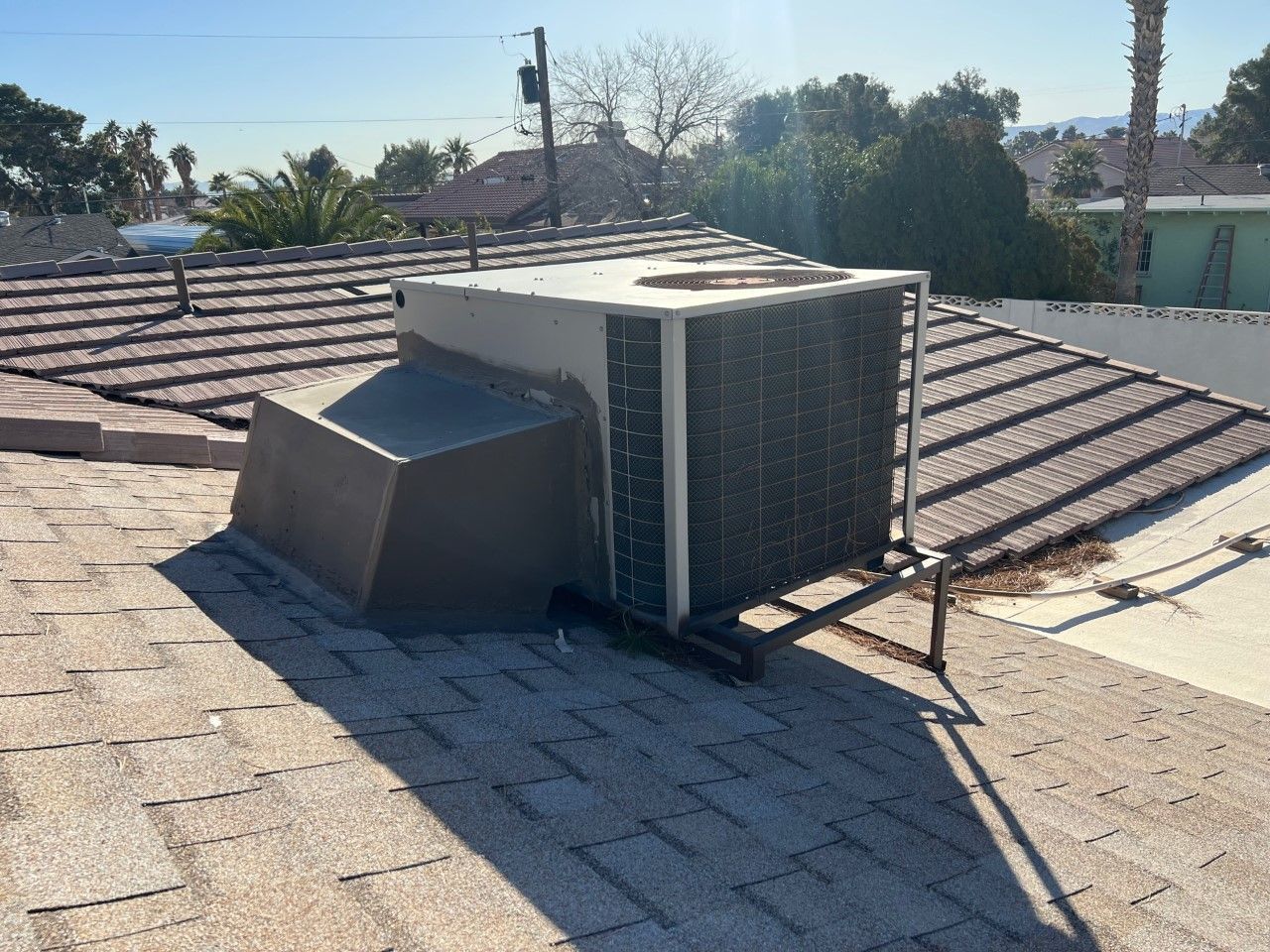 An air conditioning unit on a brown shingle roof, with a clear sky in the background.
