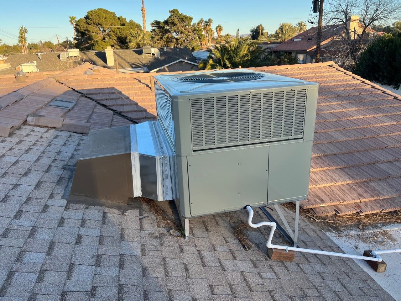 Rooftop HVAC unit, gray with vent, mounted on a residential roof, under a blue sky, during daylight.