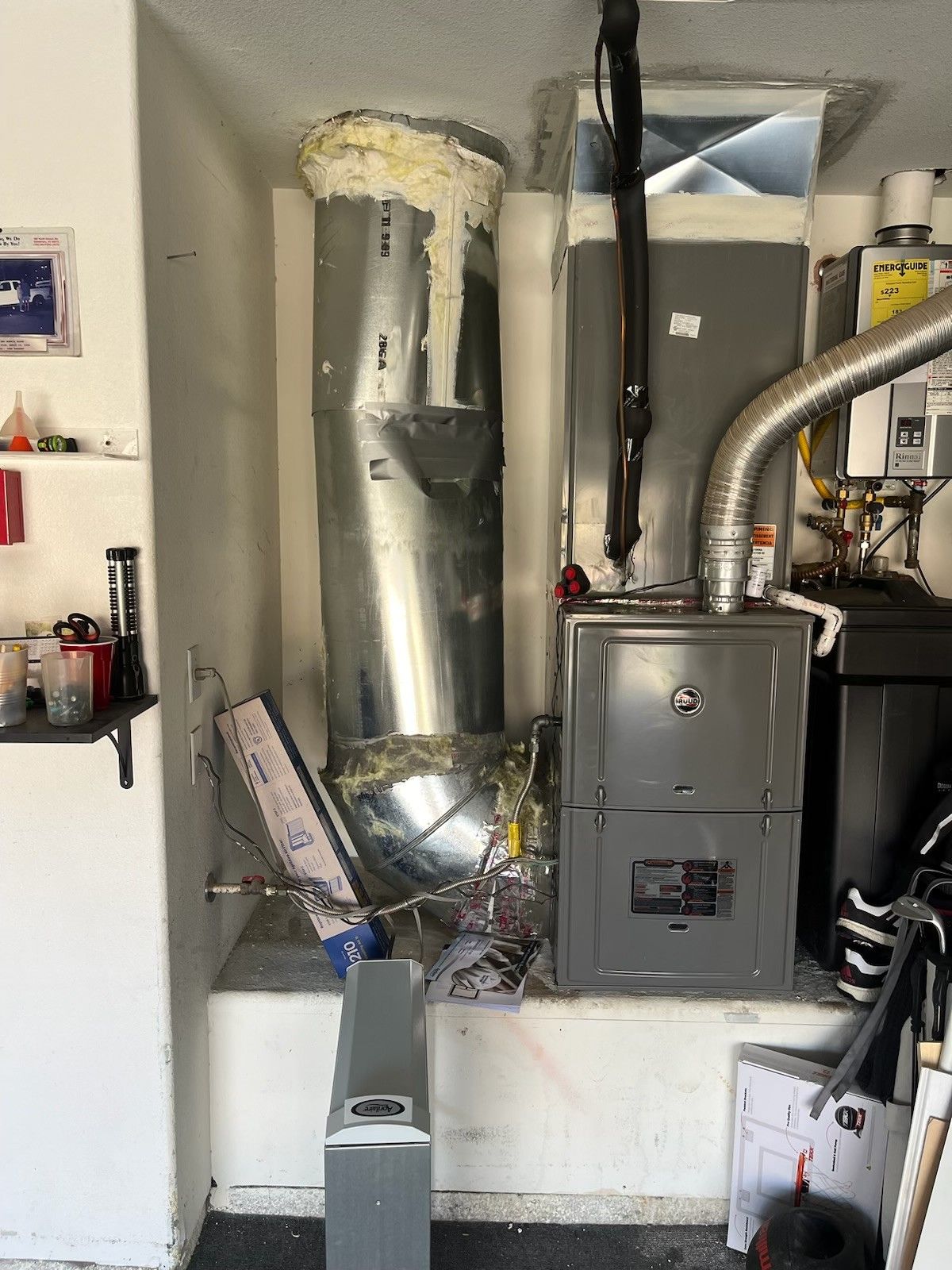 Furnace and ductwork in a garage, possibly damaged. Gray metal, white insulation, wires exposed.