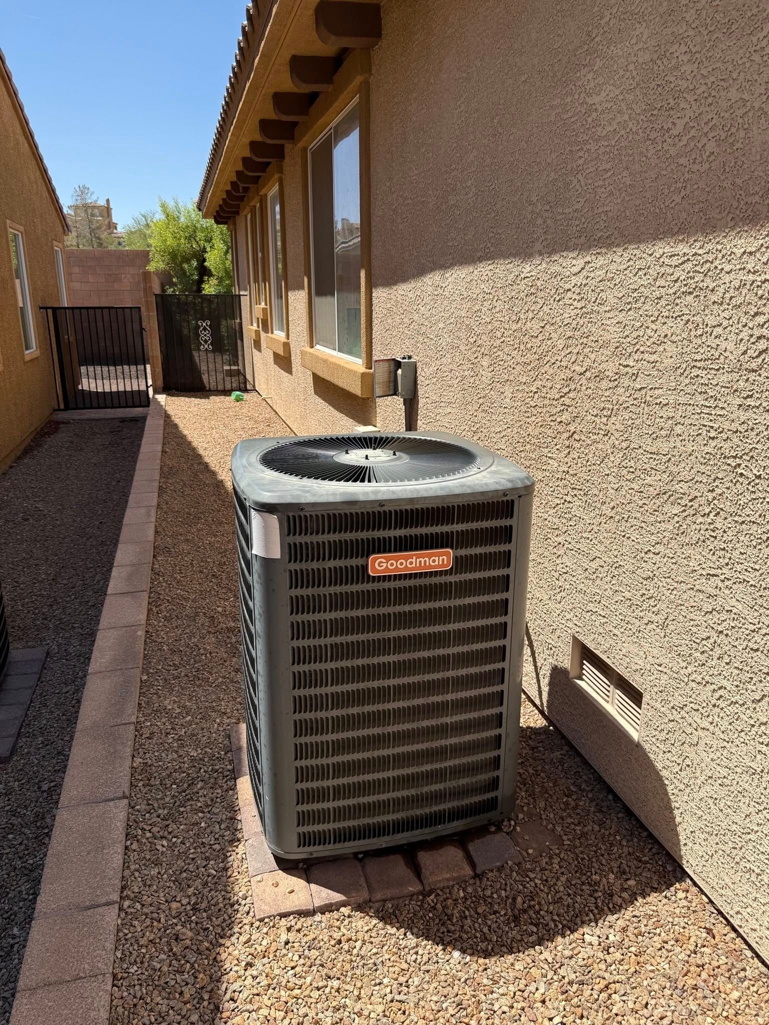 An air conditioning unit next to a stucco building on a gravel-covered pathway.