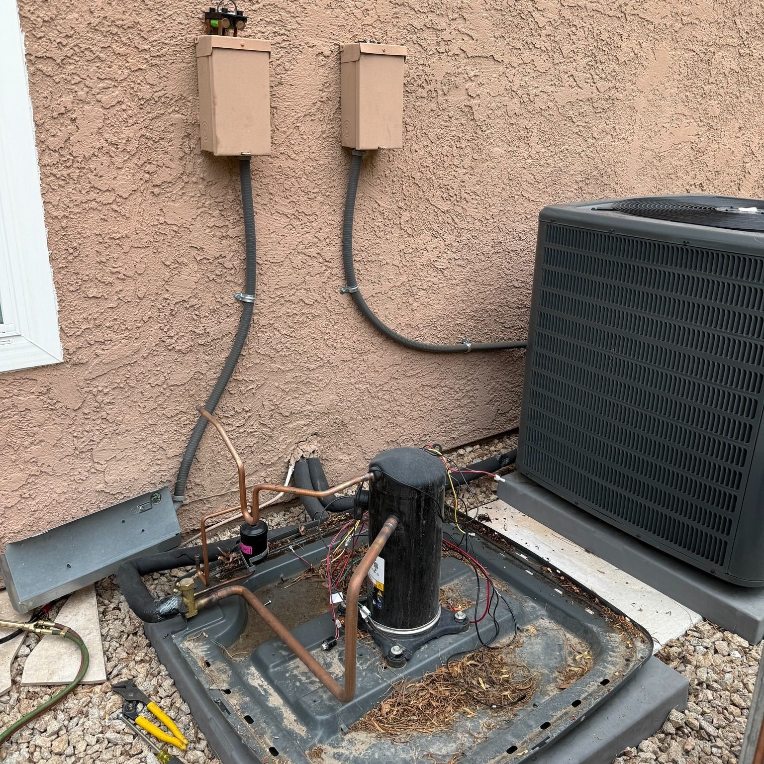 HVAC system components, including condenser, compressor, and electrical boxes, installed on a stucco wall.
