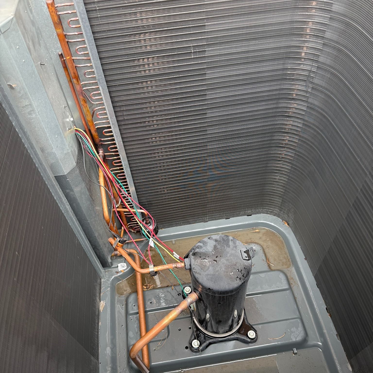 An open air conditioning unit with coils, copper tubes, and a black compressor.