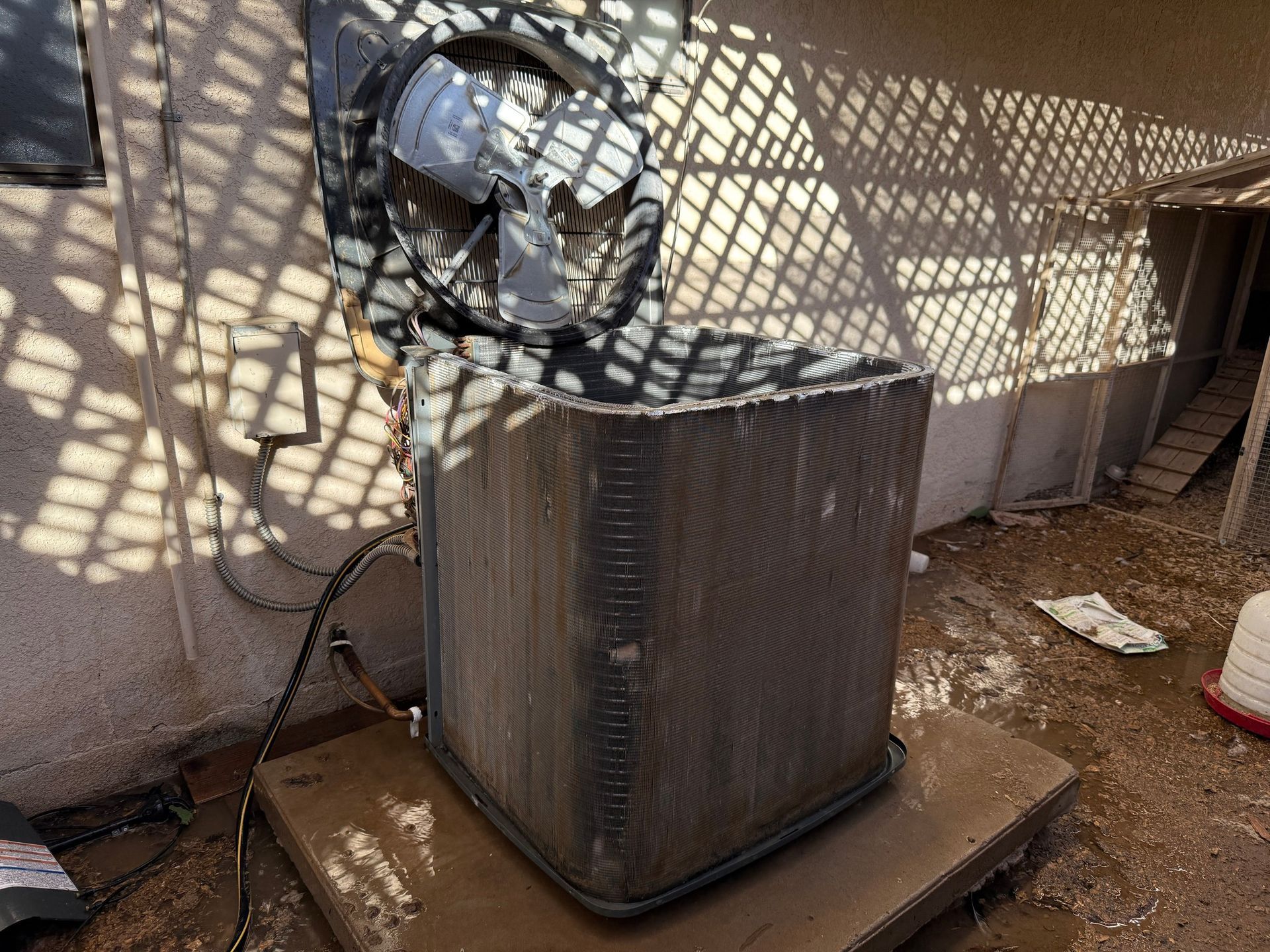 Air conditioning unit, outdoor, damaged fan, dirty condenser fins, sunlight casting shadows.