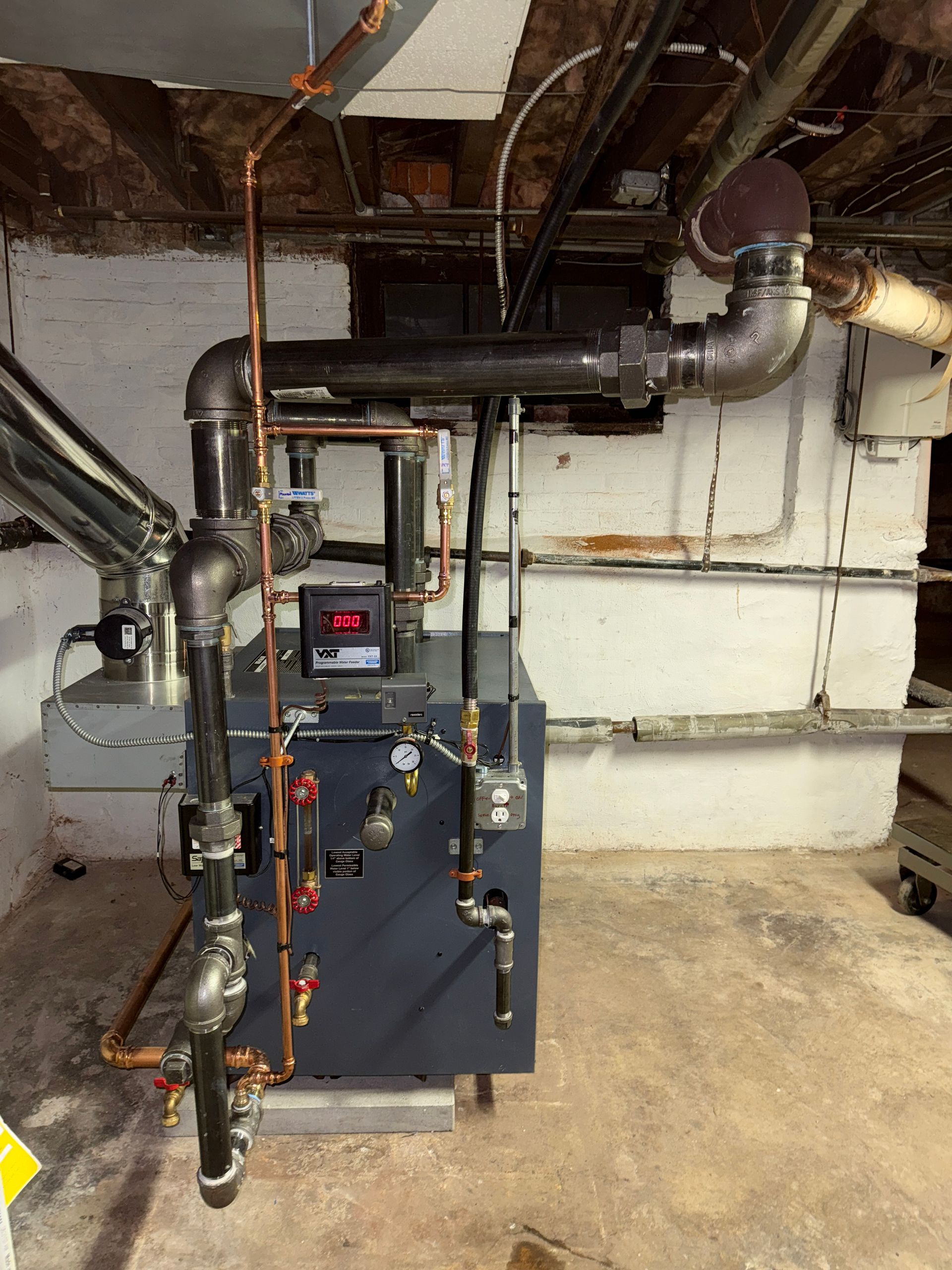 Dark blue furnace with black pipes and copper tubing in a basement.
