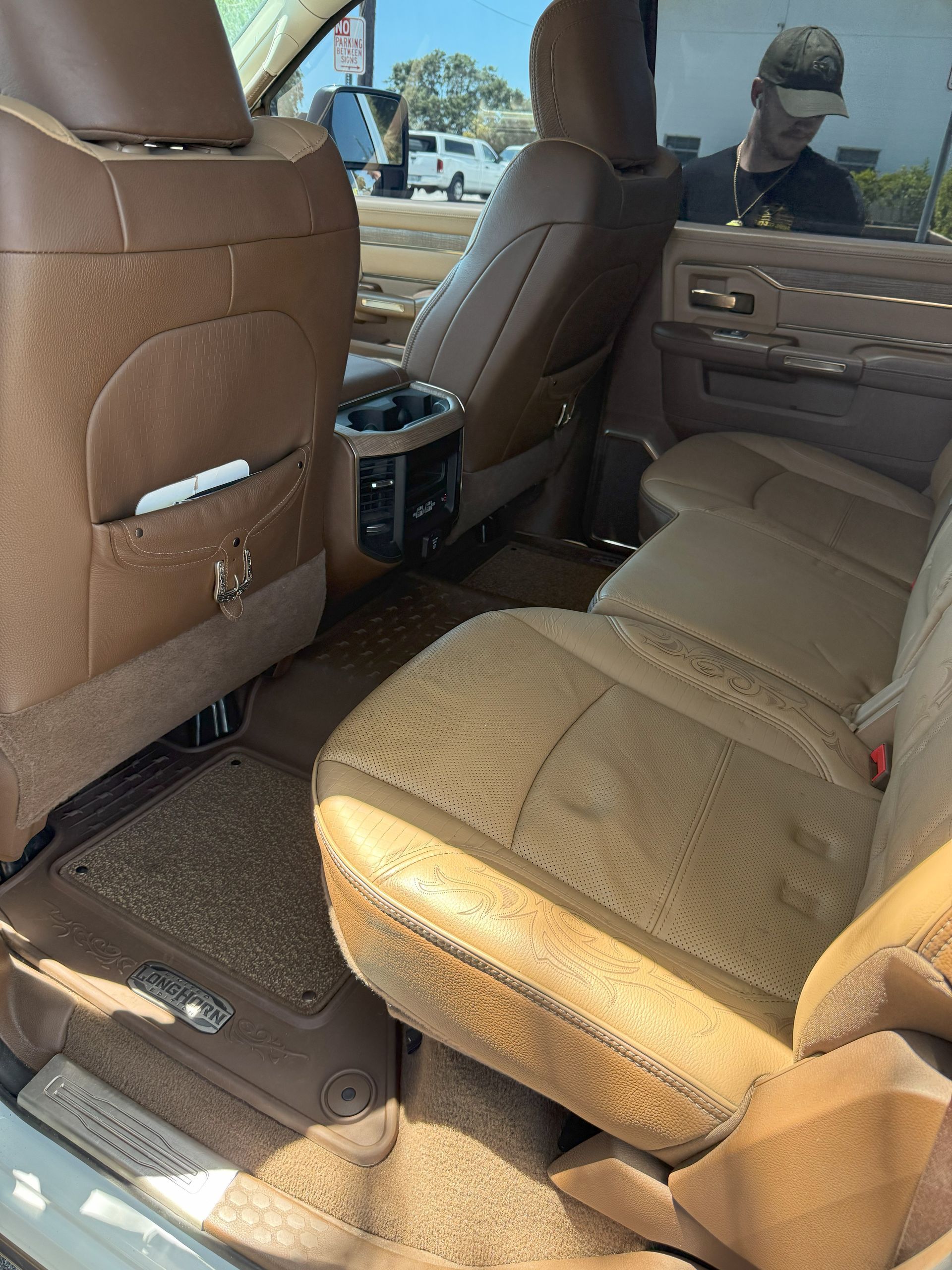 Brown leather truck interior with back seats, center console, and a person visible outside.