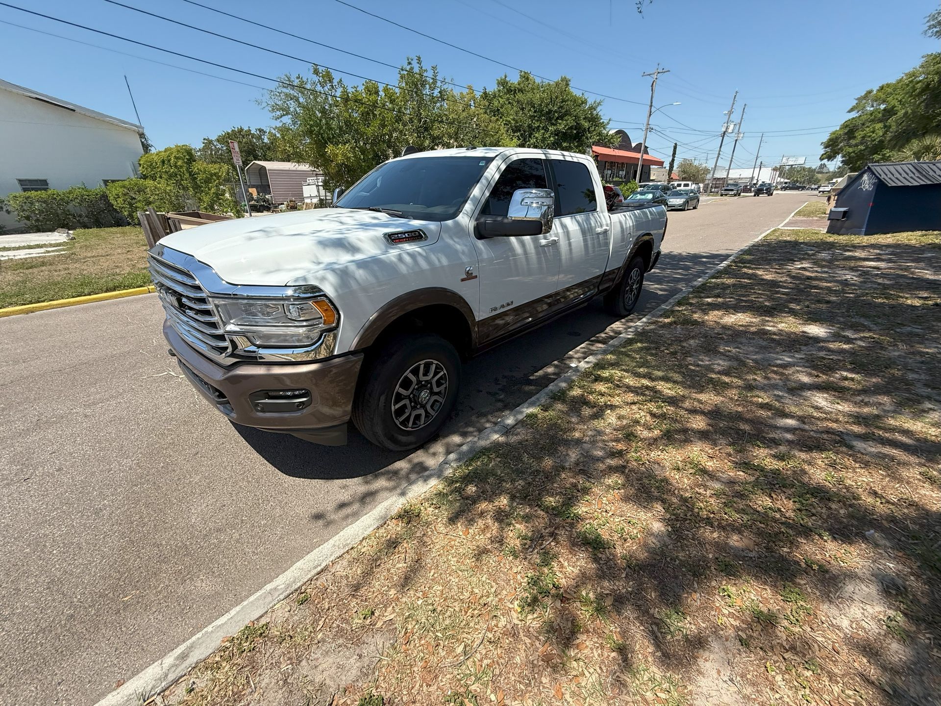White and brown Ram pickup truck parked on a road beside dry grass, sunny day.
