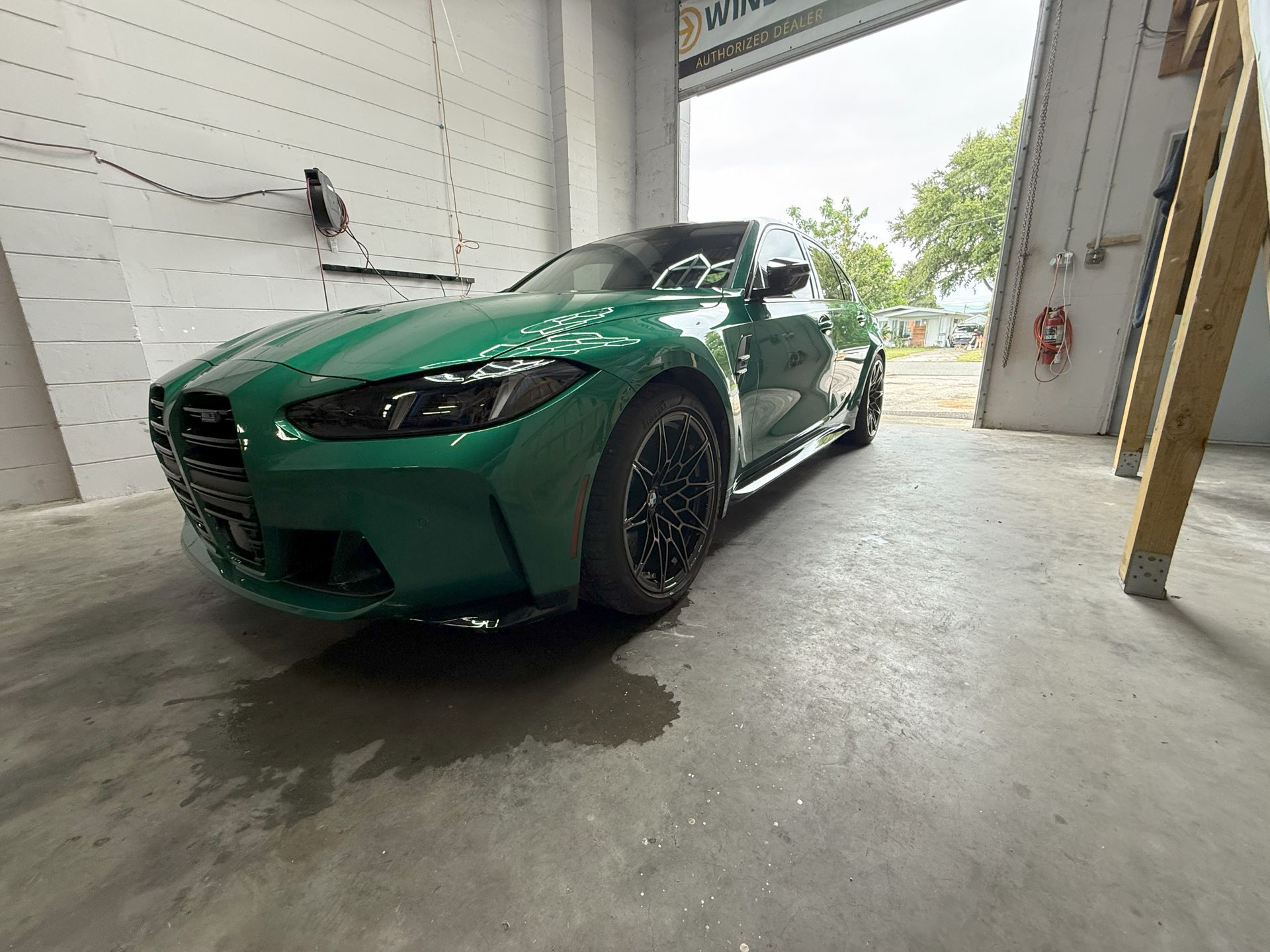 Green BMW M4 sports car inside a garage with a slightly open door.
